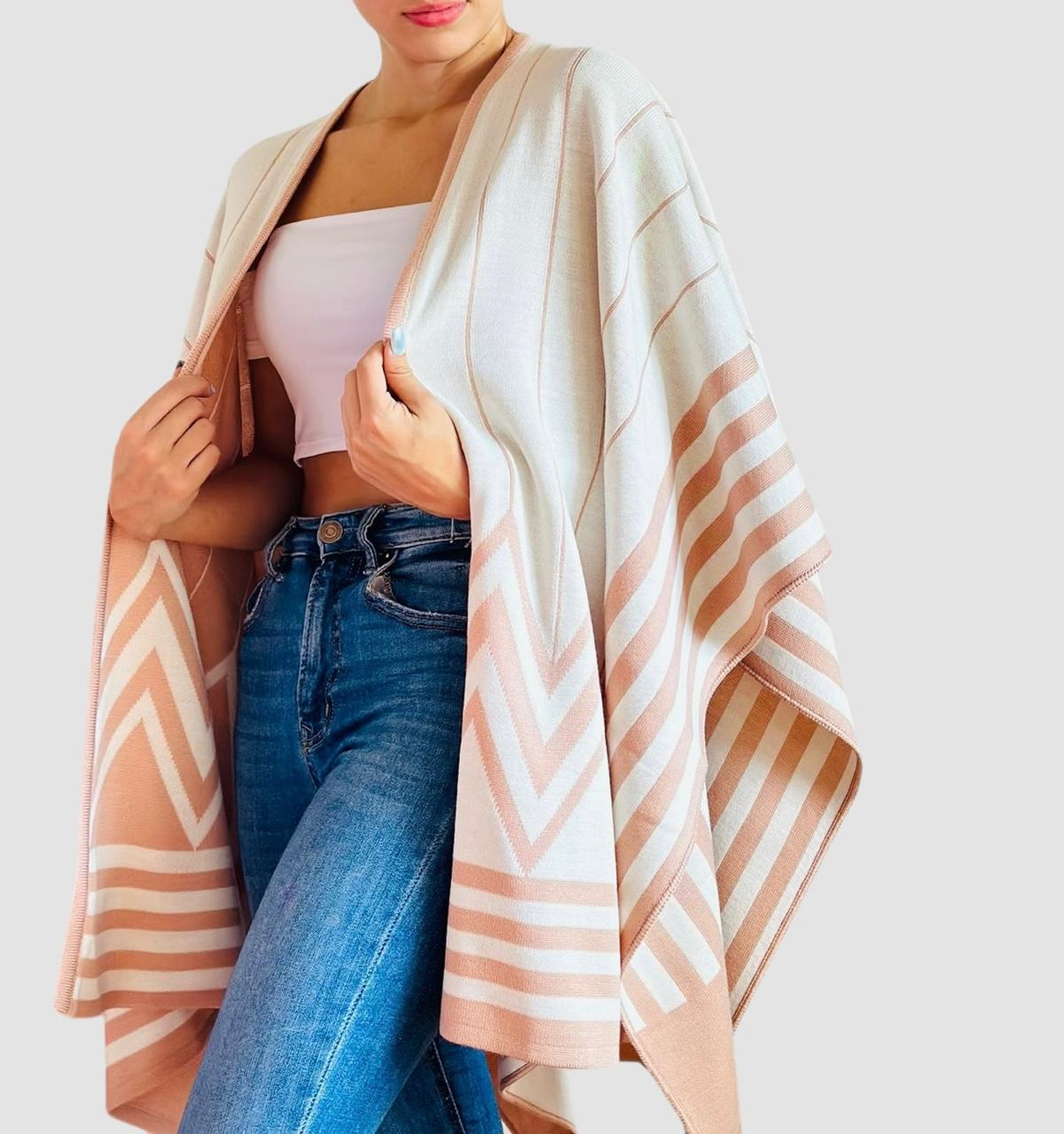Ruana doble faz tejida para mujer en tonos marfil y beige rosado, con diseño geométrico de rayas, abierta y combinada con jeans.